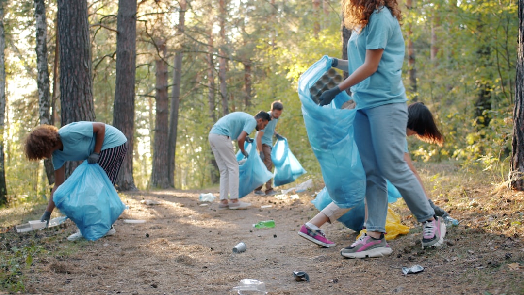 Cheerful youth eco activists are cleaning forest from garbage in summer doing voluntary work together wearing t-shirts and protective gloves. People and ecology concept.